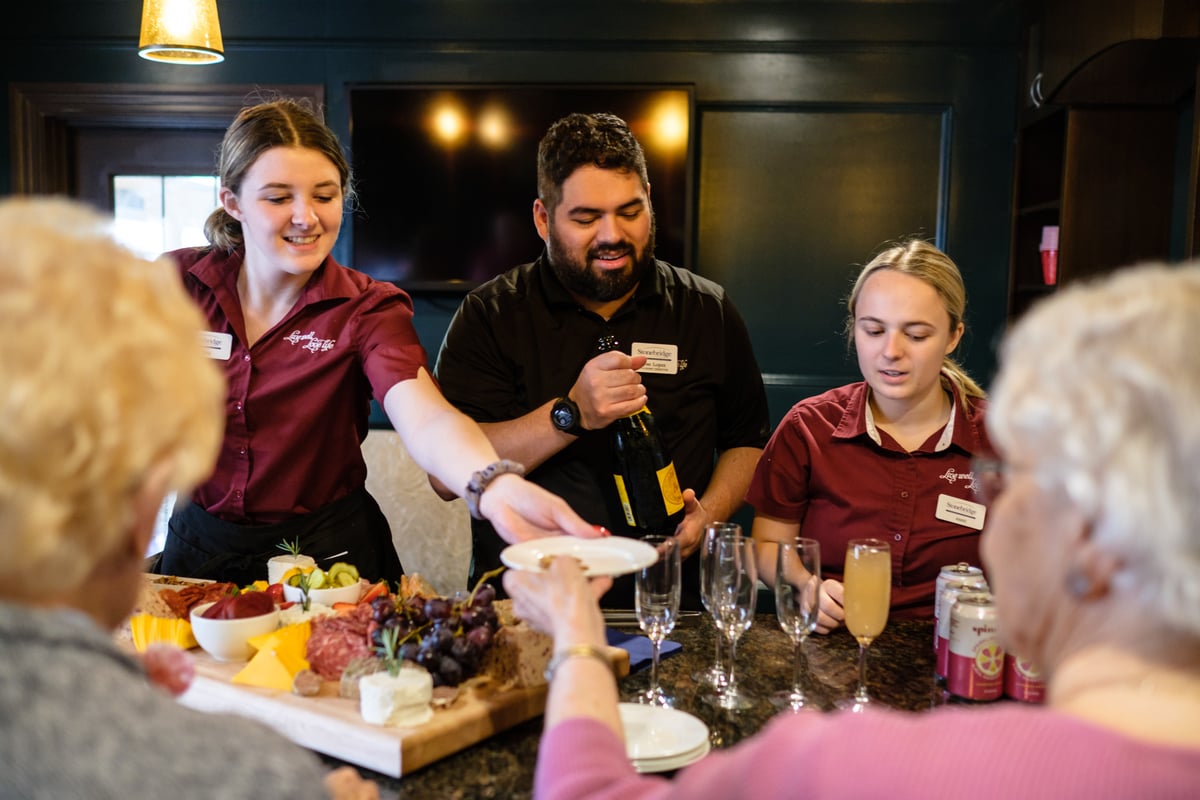Young staff workers serving wine and cheese to elderly clients